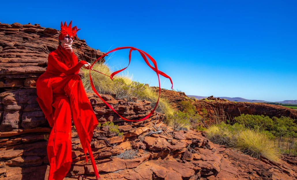 Manoeuvre stilt performer in red costume with flowing ribbons